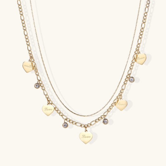 Gold layered necklace set with engraved heart pendants and crystal accents on cream background