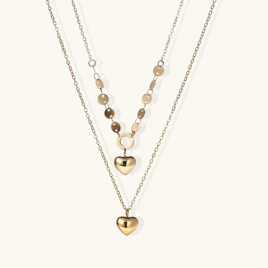 Three-layer 14K gold plated necklace with coin discs and dual heart pendants on cream background