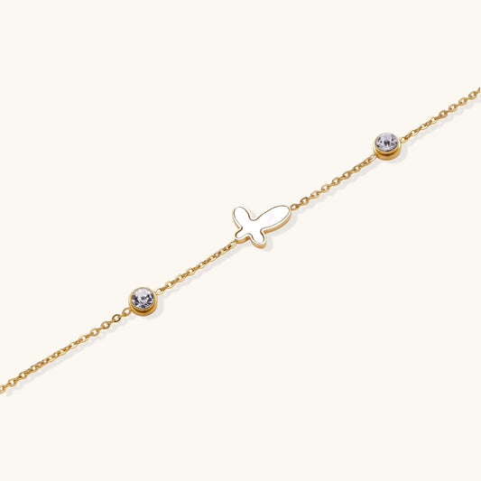 Gold chain bracelet with white mother of pearl butterfly pendant and two bezel-set crystals on cream background