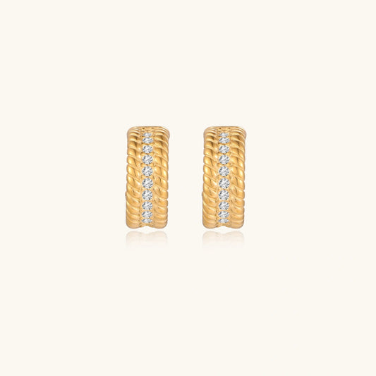 Textured gold huggie hoop earrings with raised ribbed rows creating dimensional sculptural design on cream background