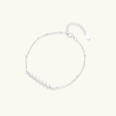 Delicate rhodium-plated silver chain bracelet with row of small baroque pearls centered on white background.