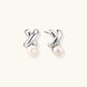 Rhodium-plated silver earrings with twisted X design and freshwater pearl drops on beige background