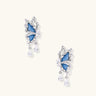 Silver butterfly earrings with blue denim fabric wings and dangling teardrop crystals on cream background