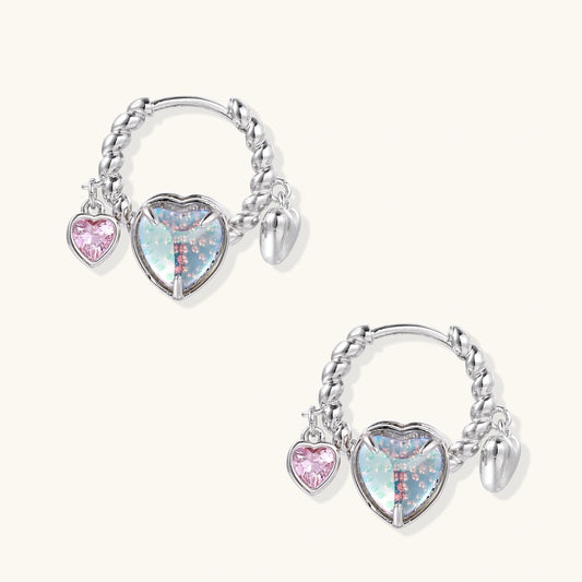 Silver chain hoop earrings with iridescent opal heart charms and pink zirconia accents on white background