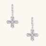 Ornate white gold-plated cross earrings with baguette-cut zirconia stones and twisted leverback hooks on beige background