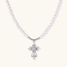 White pearl necklace with ornate silver cross pendant featuring zirconia crystals on cream background.