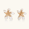 White enamel tropical flower earrings with sculptural gold-plated center and organic petal design on cream background