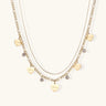 Gold layered necklace set with engraved heart pendants and crystal accents on cream background