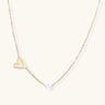 Delicate gold necklace with open heart charm and white pearl bead on fine chain against cream background