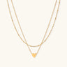 Delicate double-chain gold necklace with tiny heart pendant on cream background