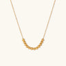 Delicate gold-plated necklace with graduated spherical beads forming gentle smile curve on beige background