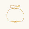 Delicate gold chain bracelet with minimalist bar and centered knot detail on cream background