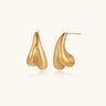 Organic sculptural gold stud earrings with fluid matte finish on cream background