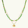 Layered necklace with green stone beads, gold spacers, white accents, and protective eye pendant on cream background.